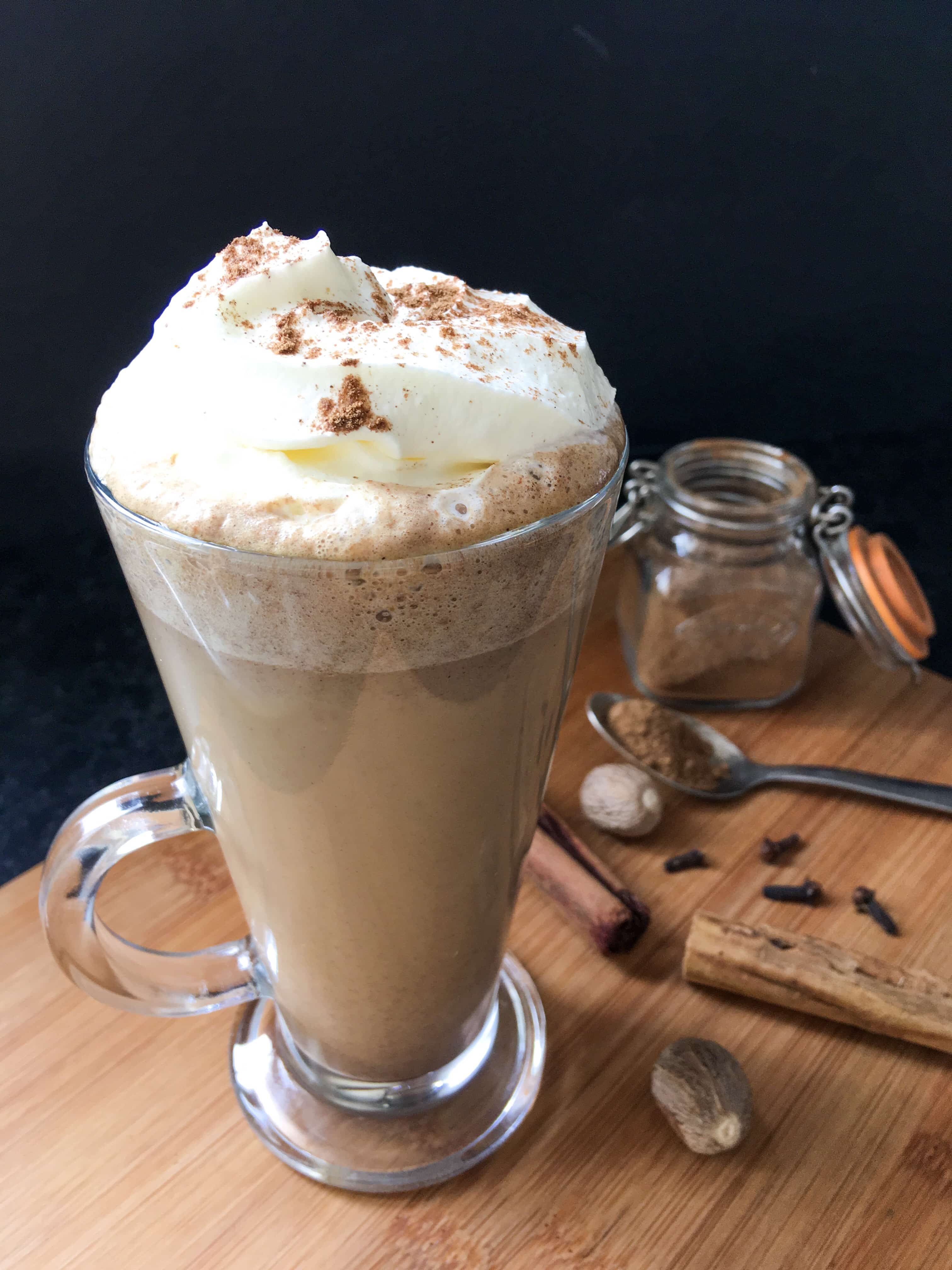 A homemade pumpkin spice latte in a tall latte glass on a wooden board. 