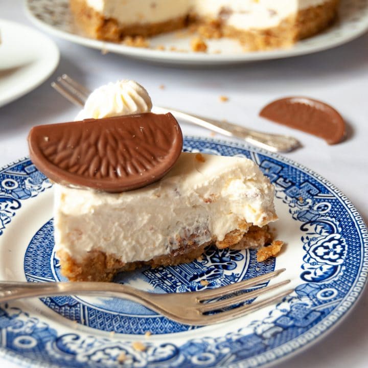 A slice of no bake Terry's chocolate orange cheesecake on a blue Willow pattern plate. The cut cheesecake can be partially seen in the background.