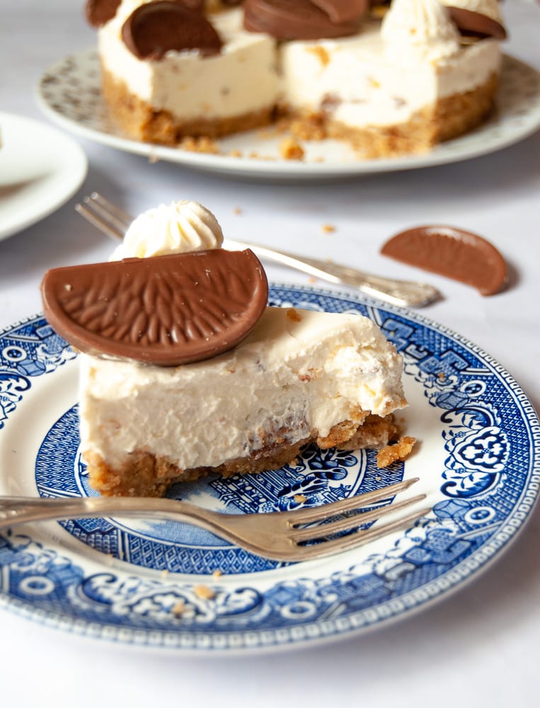 A slice of no bake Terry's chocolate orange cheesecake on a blue Willow pattern plate. The cut cheesecake can be partially seen in the background.