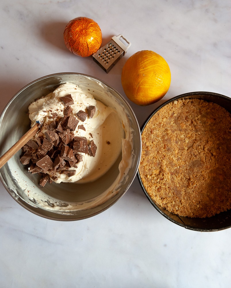 A bowl of cheesecake filling with chopped Terry's chocolate orange with a springform tin with a digestive biscuit cheesecake base.