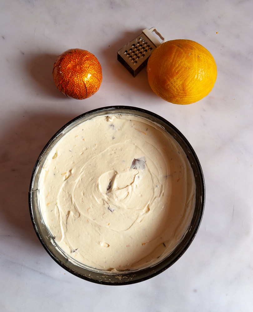 A no bake chocolate orange cheesecake in a springform tin on a white marbled background