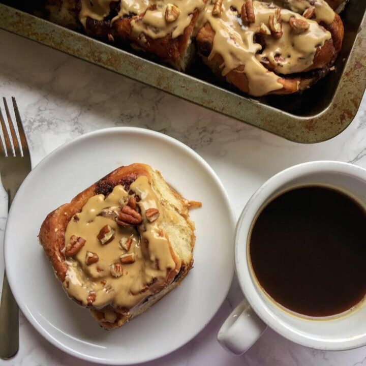 A Mocha swirl sticky bun on a white plate beside a cup of black coffee.