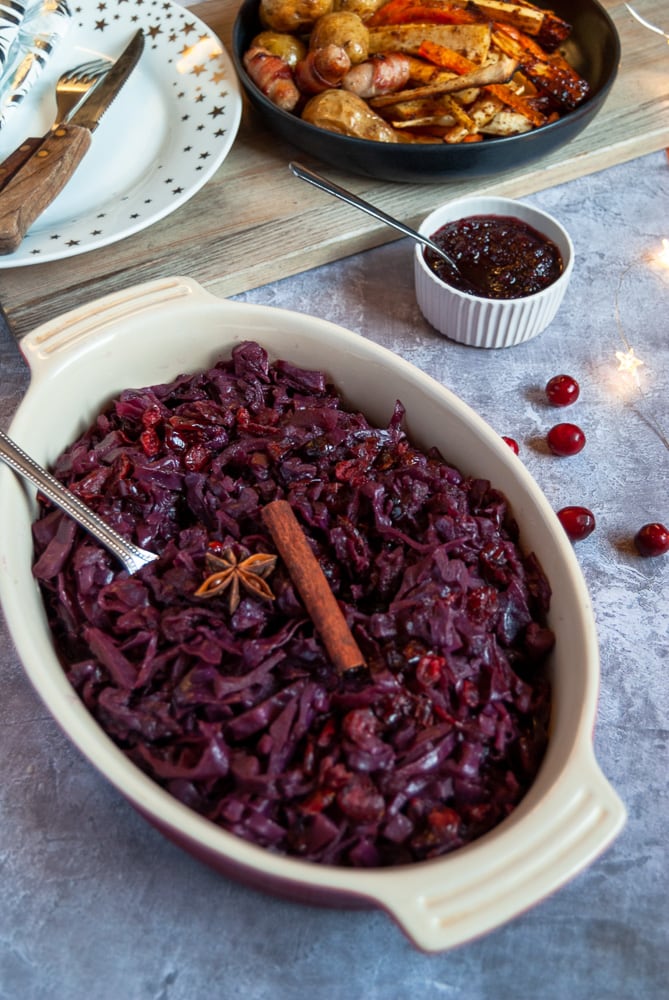 A casserole dish of Christmas spiced red cabbage. A bowl of roasted potatoes, parsnips and carrots are in the background