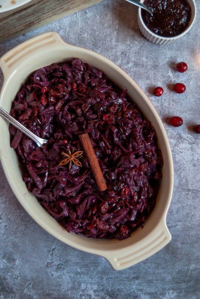 A casserole dish of braised red cabbage. A pot of cranberry sauce and fresh cranberries can also be seen.