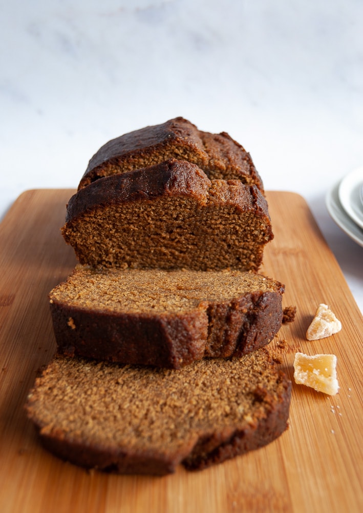 A face on photo of a partially sliced gingerbread loaf cake on a wooden chopping board.