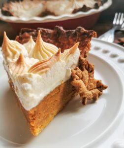 A slice of pumpkin pie on a white plate with a maple leaf shaped cookie.