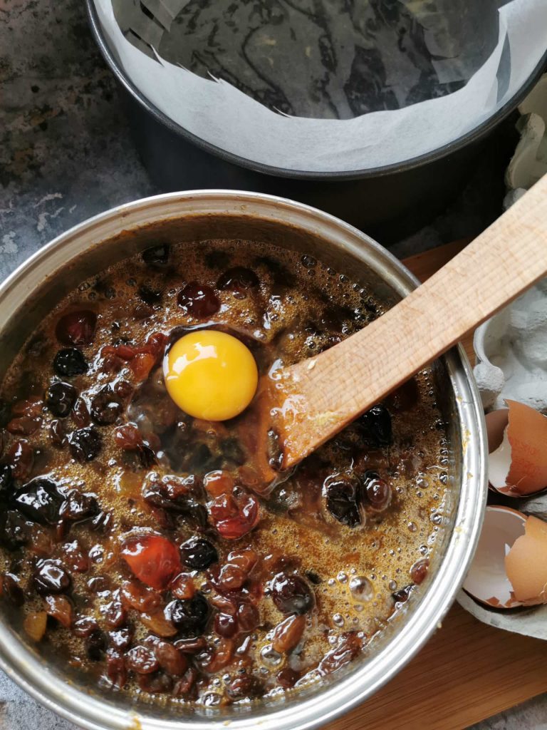 Eggs being added to a fruit cake batter in a saucepan.