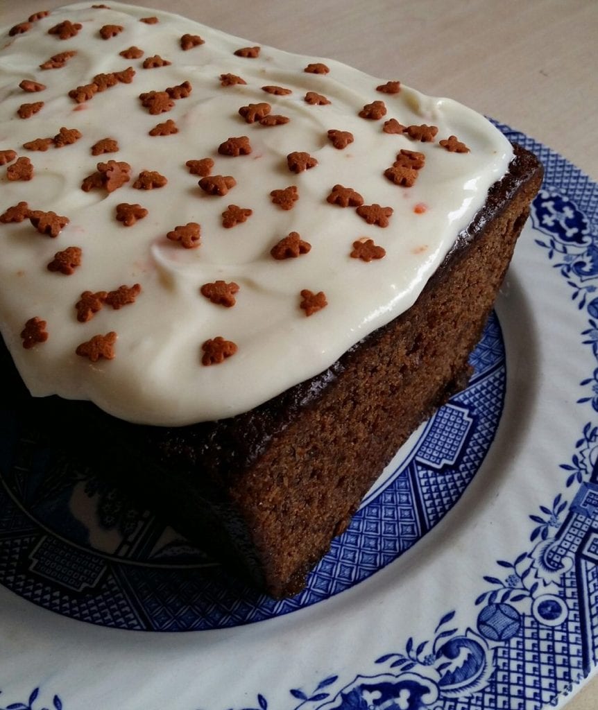 A gingerbread loaf cake topped with orange cream cheese icing and decorated with gingerbread men sprinkles.