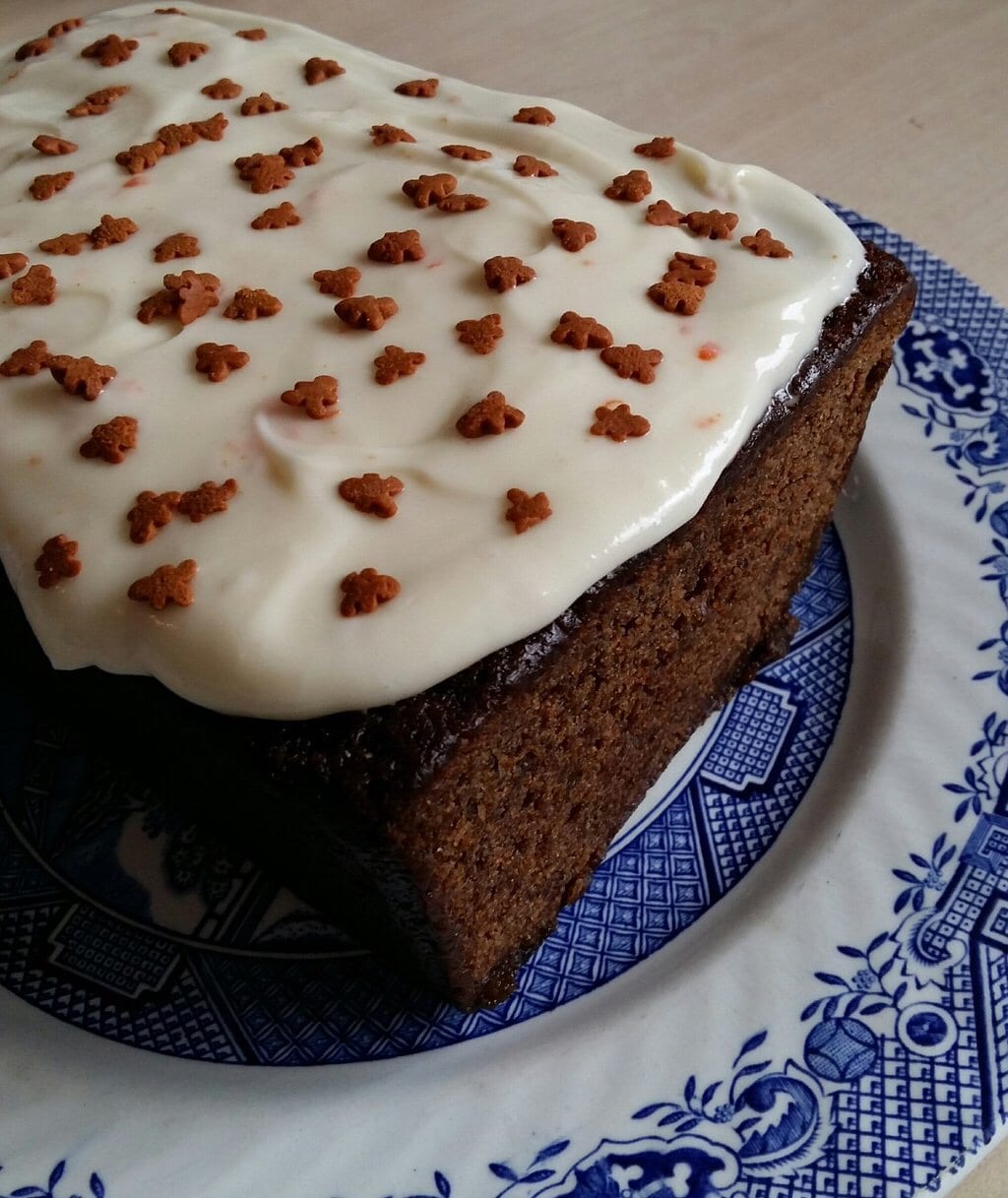 A gingerbread cake topped with orange cream cheese icing and decorated with gingerbread men sprinkles.