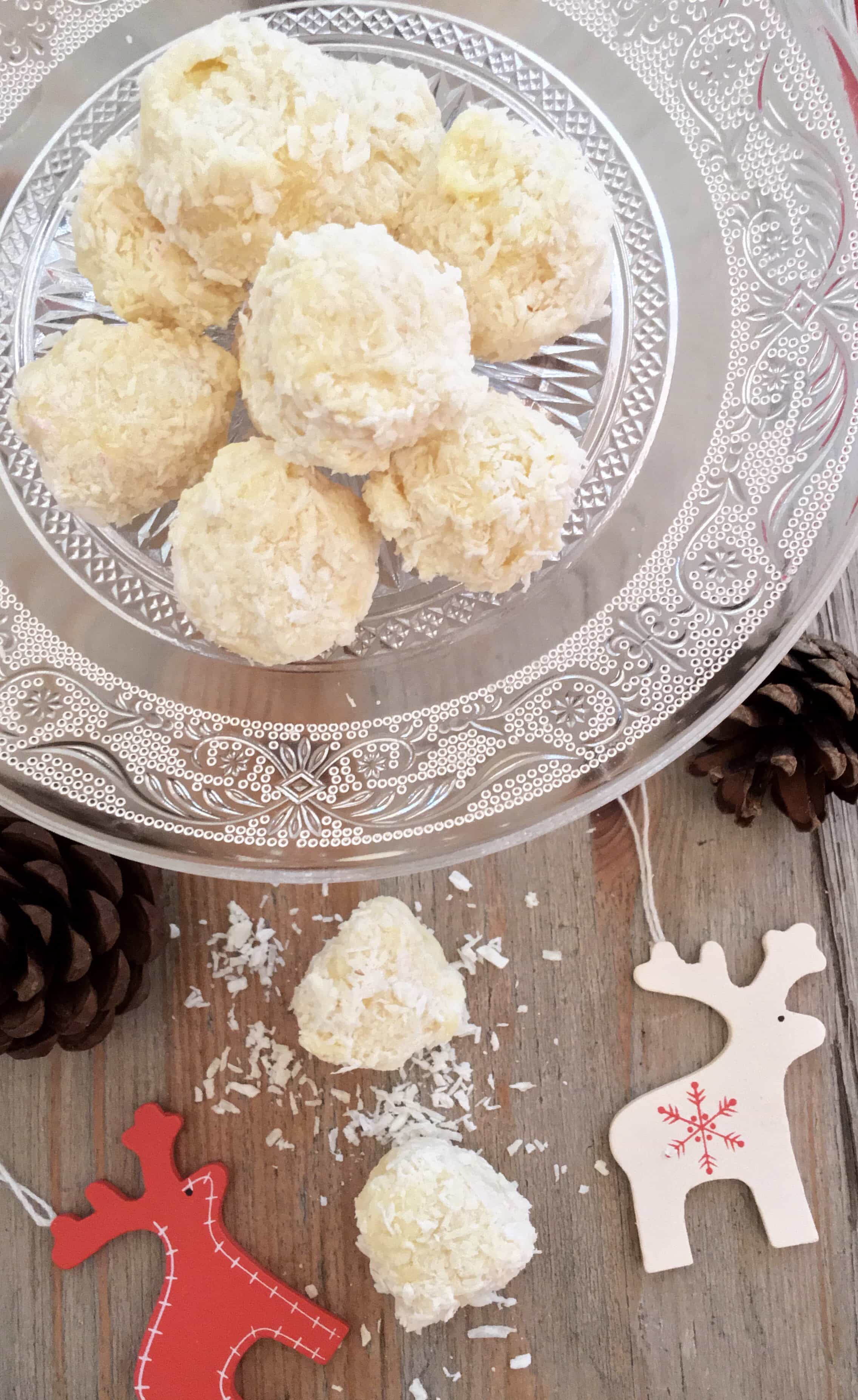 White chocolate and coconut truffles on a mini glass cake stand. Christmas decorations are placed around the plate for a festive look. 