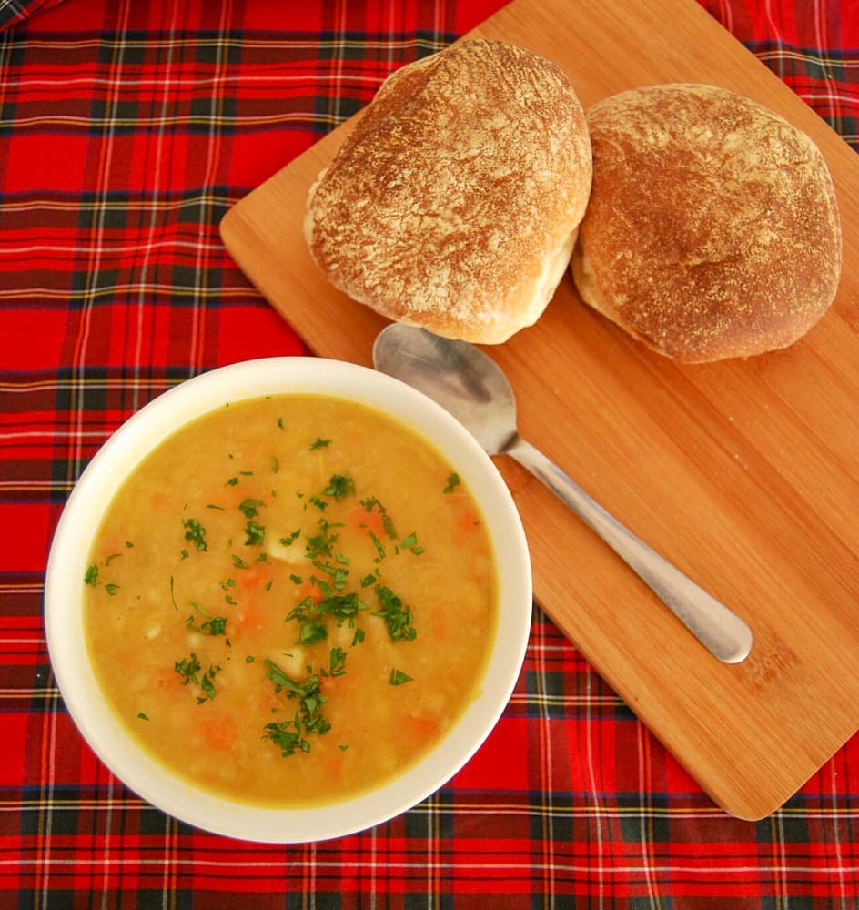 A bolw of tattie soup with bread rolls on a tartan background