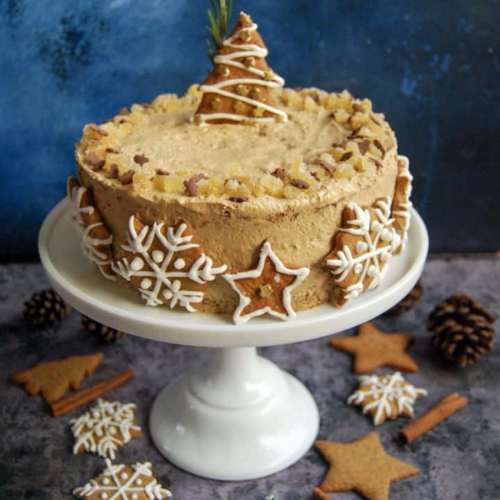 a gingerbread latte cake decorated with iced gingernbread biscuits on a white cake stand