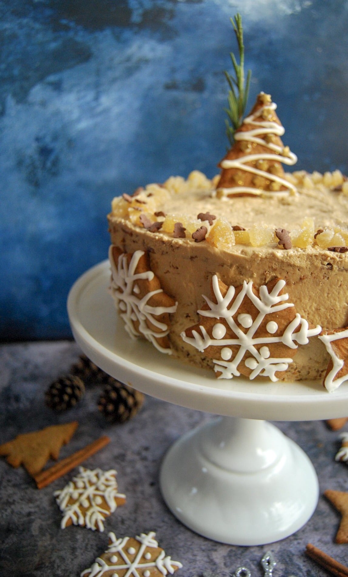 A close up picture of a gingerbread latte cake on a white cake stand. The cake is frosted with Biscoff buttercream and decorated with iced ginger biscuits.