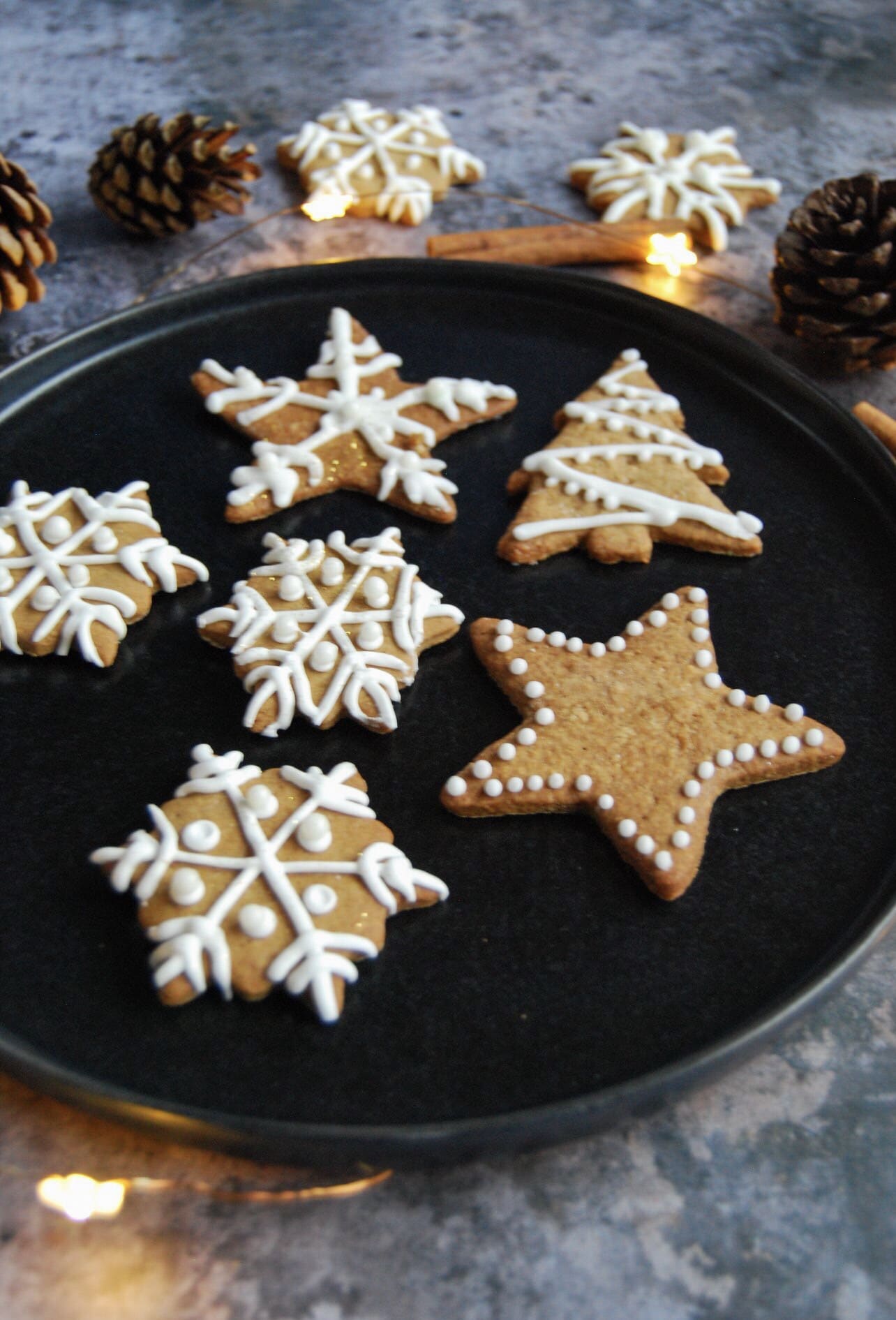 A close up picture of Christmas gingerbread biscuits decorated with white icing on a black plate