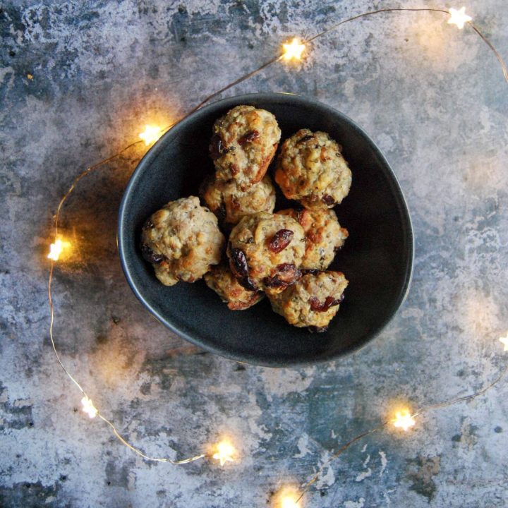 a black bowl filled with sausage and sage stuffing balls studded with cranberries surrounded by gold fairy lights on a grey background.