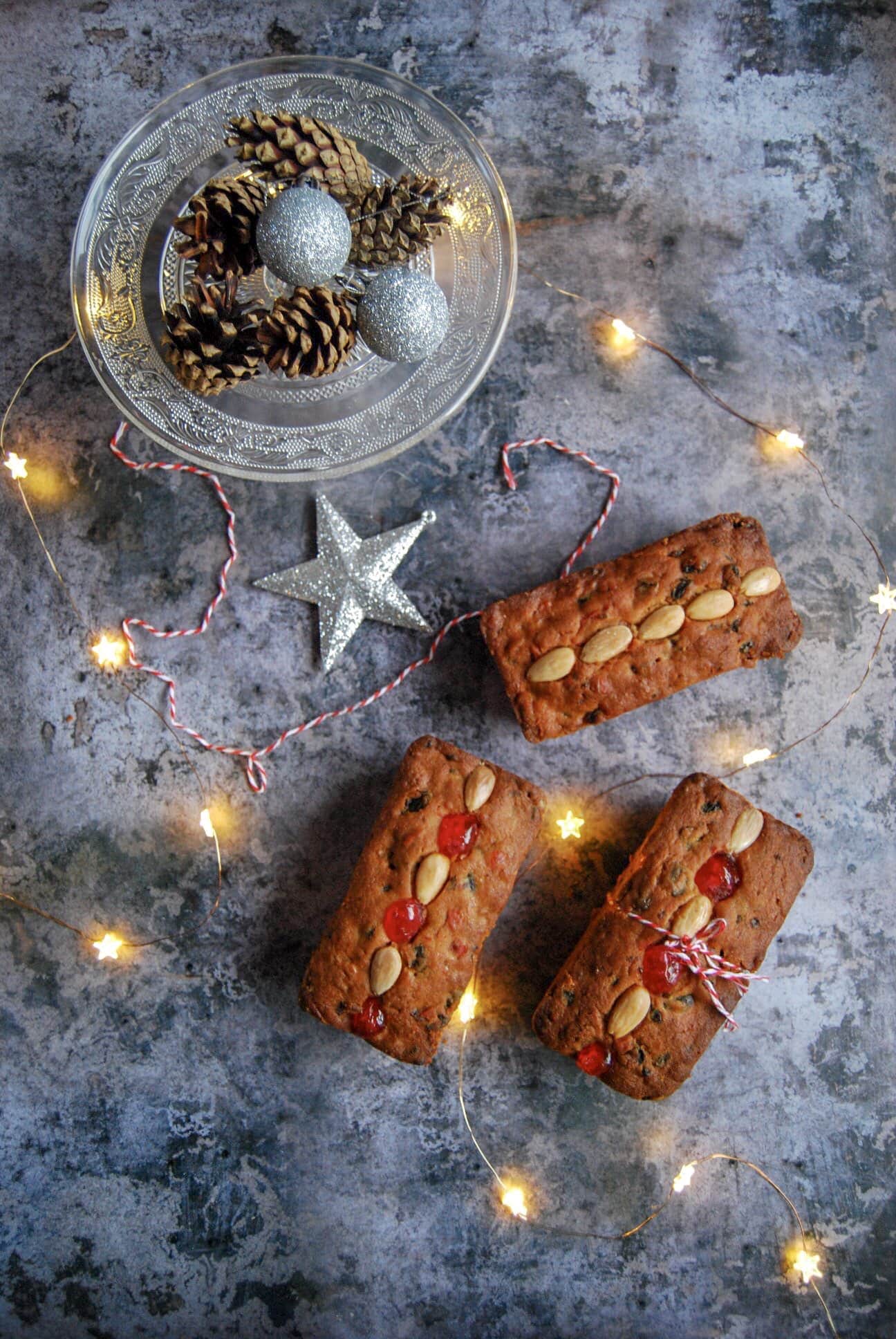 Three Mincemeat Loaf Cakes on a grey background with twinking fairy lights and silver Christmas decorations