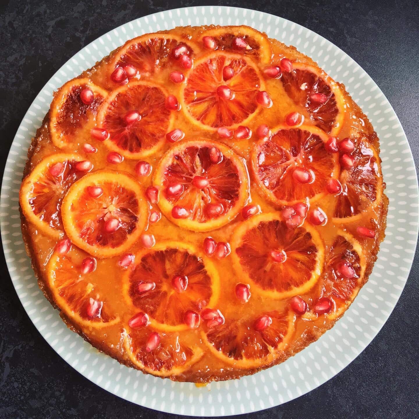 A flat lay photo of a blood orange blossom pomegranate cake on a white and green plate.