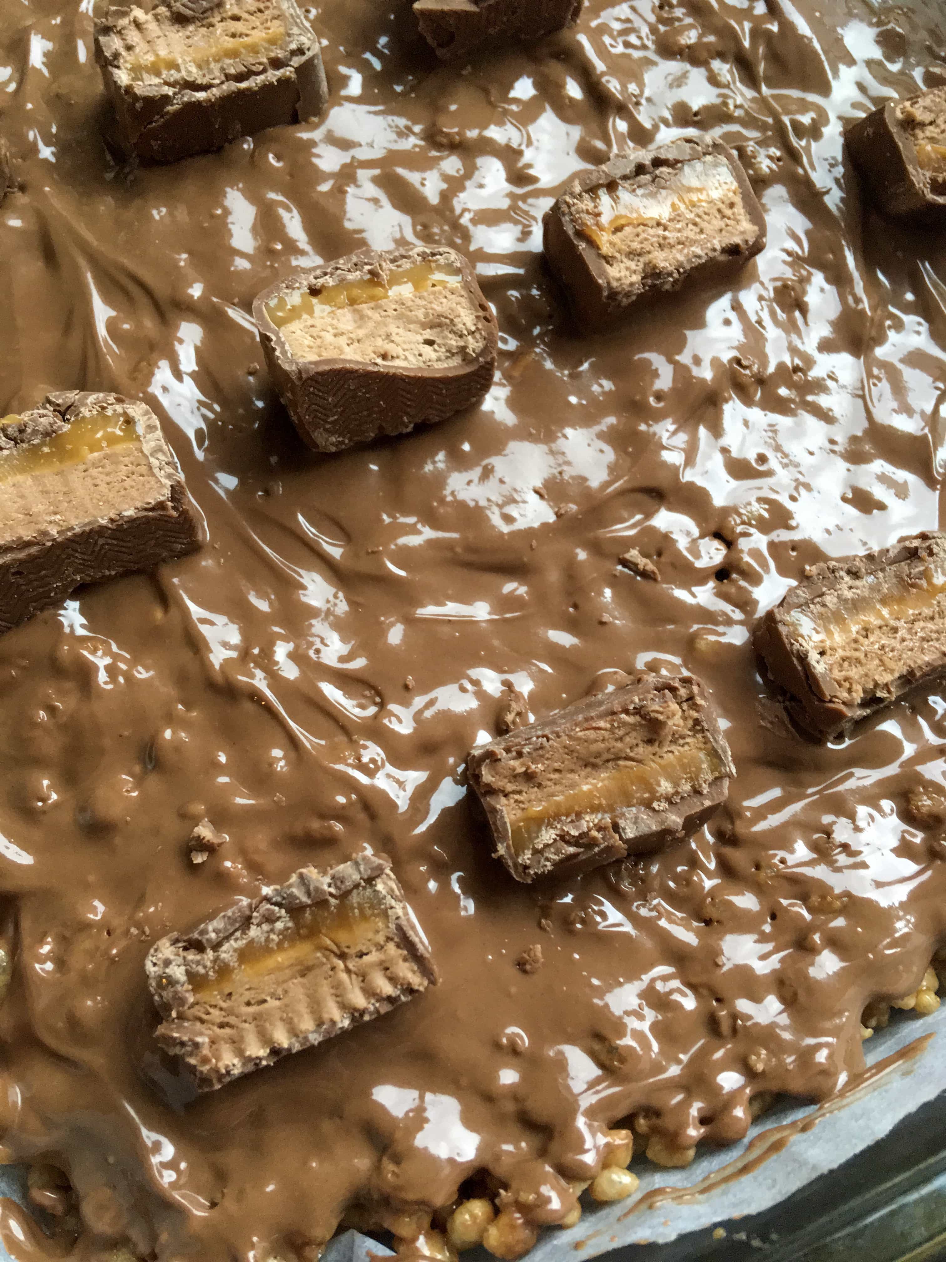 A close up photo of a Mars Bar Cake covered in milk chocolate and chopped Mars Bars