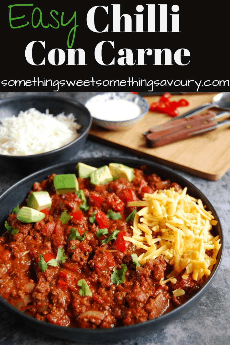 A Pinterest pin with the words "Easy Chilli Con Carne" and a photo of a bowl of chilli with grated cheese and avocado. A bowl of rice, sour cream and red chillies can be seen in the background.
