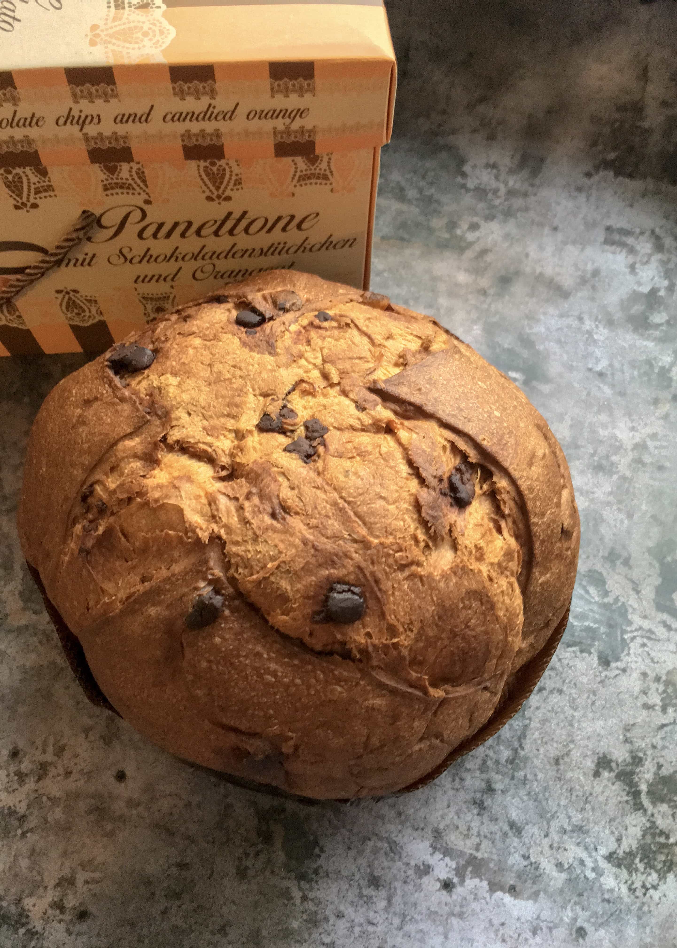 a large chocolate chip panettone with an orange and brown box on a grey backdrop