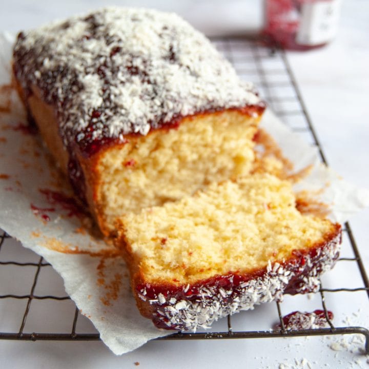 A coconut and raspberry jam loaf cake on a wire rack, with a jar of raspberry jam in the background