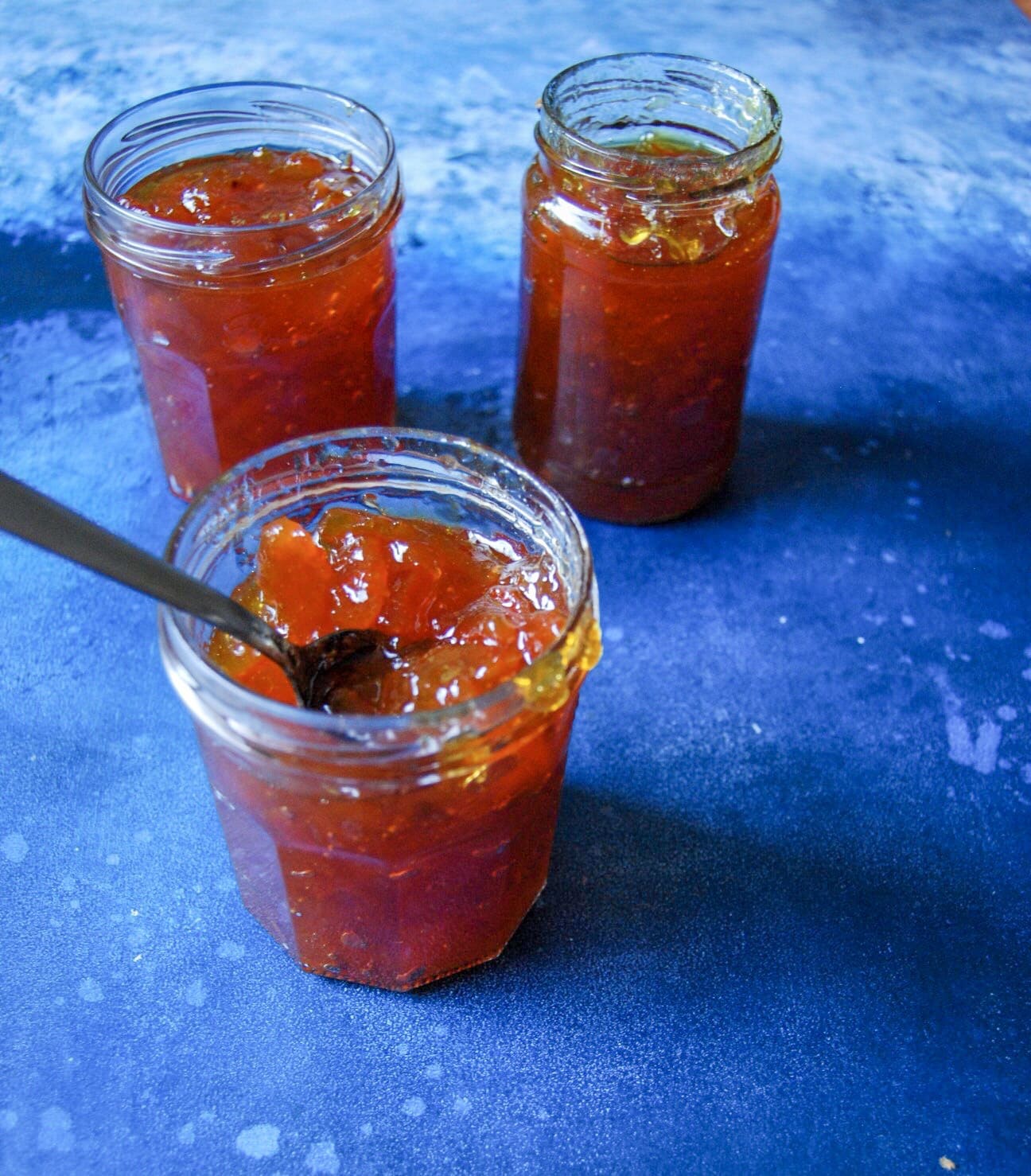 Three jars of orange marmalade on a blue background. 