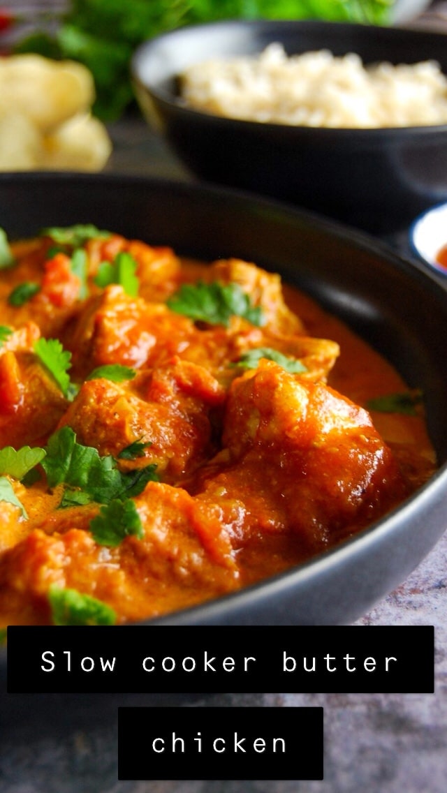 A black stoneware plate of slow cooker butter chicken sprinkled with chopped coriander with bowls of rice, mango chutney and poddadoms in the background.