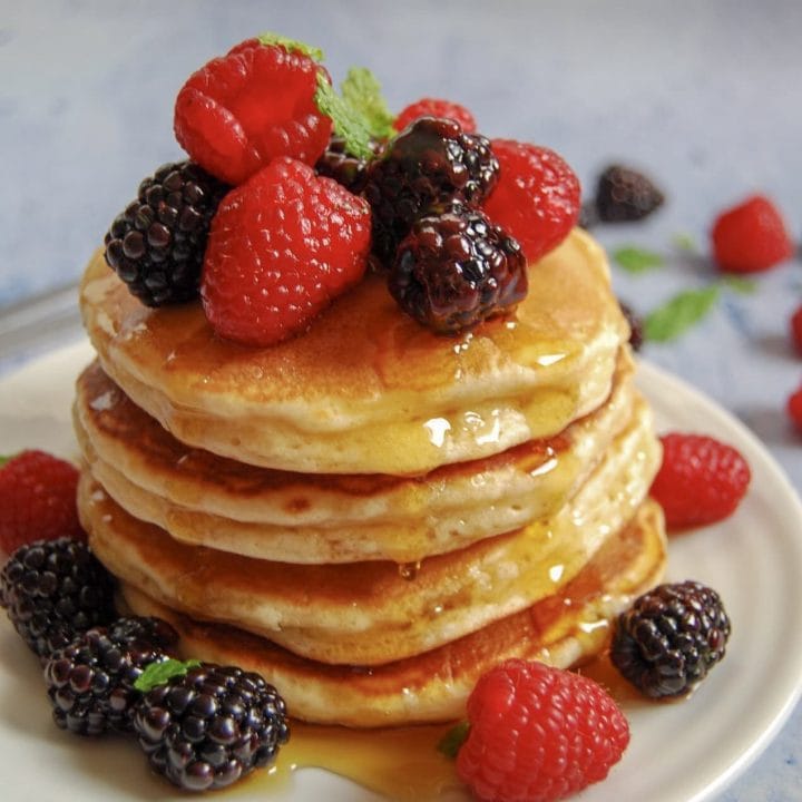 A stack of fluffy American pancakes with fresh berries, dripping in maple syrup