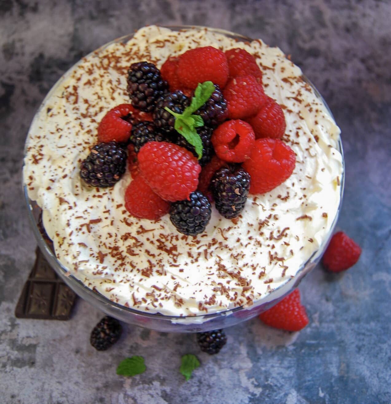 an overhead picture of a chocolate brownie trifle decorated with whipped cream and berries in a glass bowl