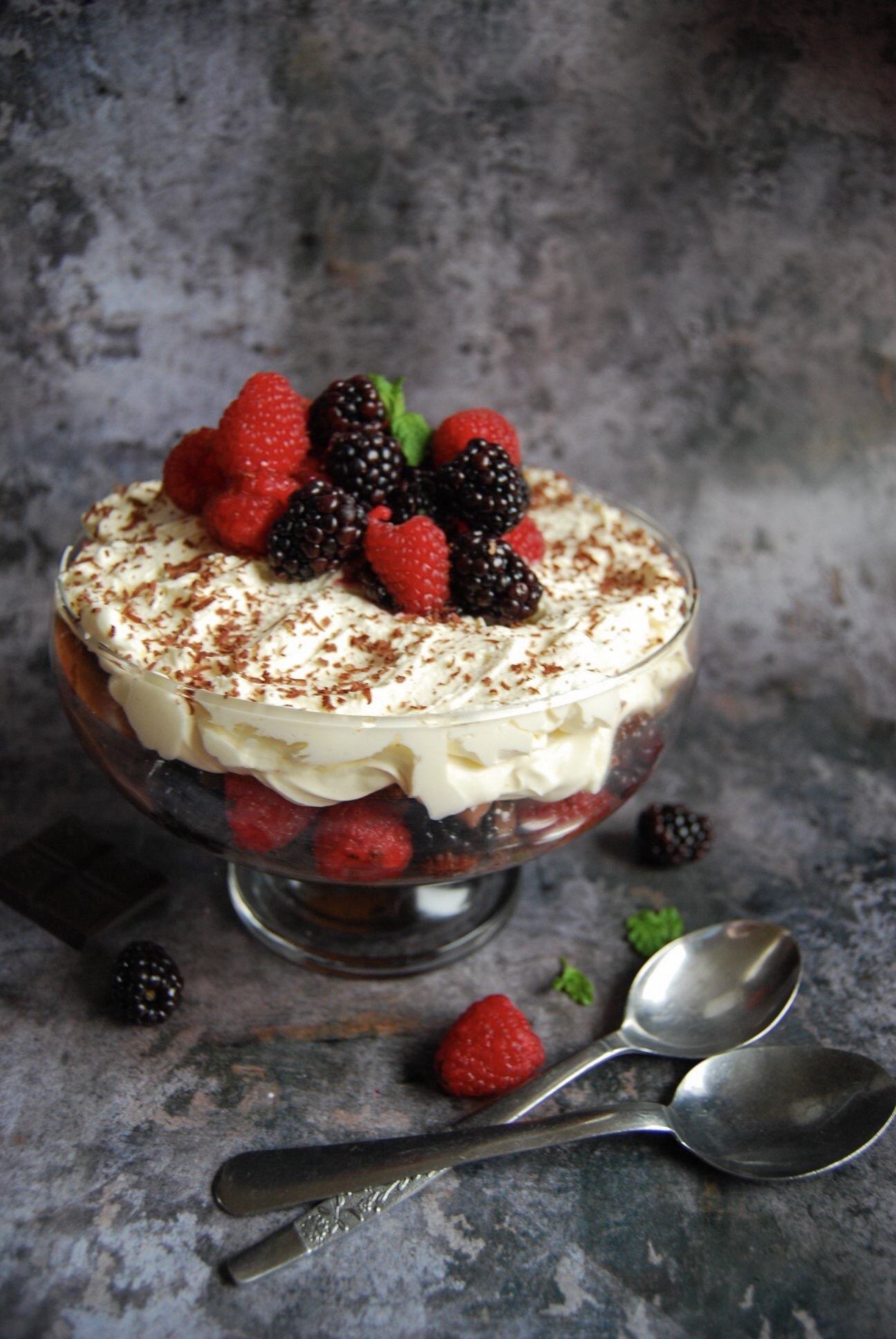 A chocolate brownie trifle topped with whipped cream, grated chocolate and fresh berries in a glass bowl