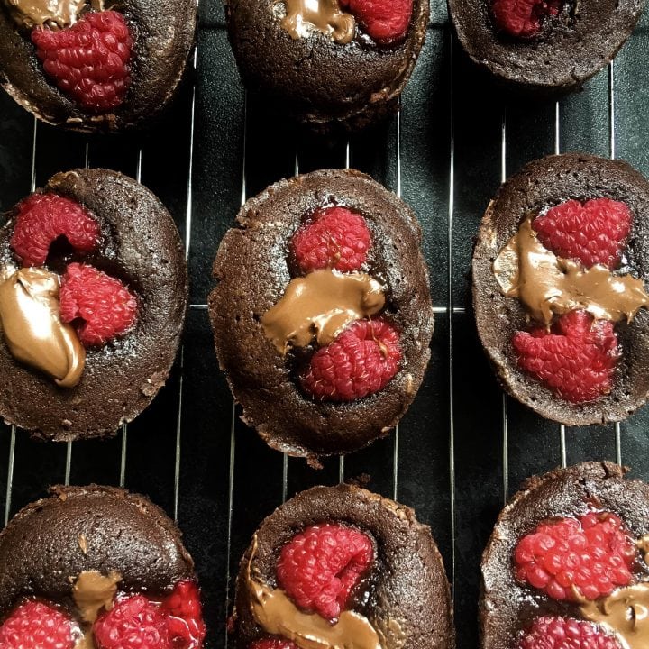 Nine little round chocolate cakes topped with fresh raspberries and hazelnut chocolate spread on a sliver wire rack