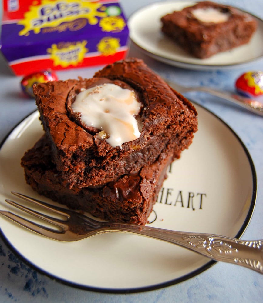 Two cadbury creme egg brownies on a white and black plate. A box of creme eggs can be seen in the background.