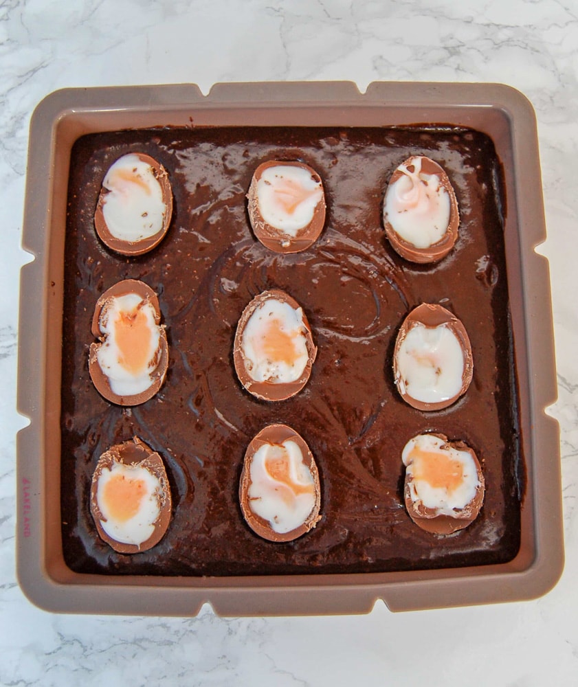 A square tray of unbaked creme egg brownies on a marbled white background.