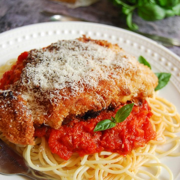 A close up picture of Chicken Milanese with Tomato sauce and spaghetti on a white plate.