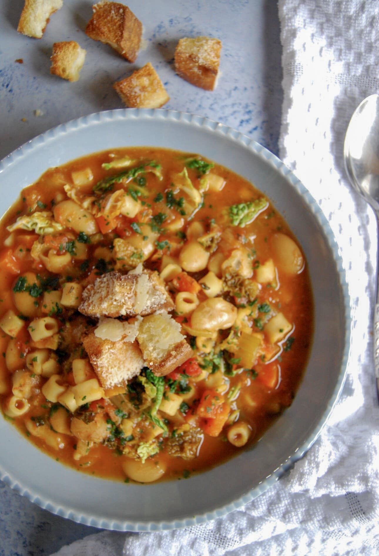 A bowl of minestone soup with croutons on a light blue backdrop