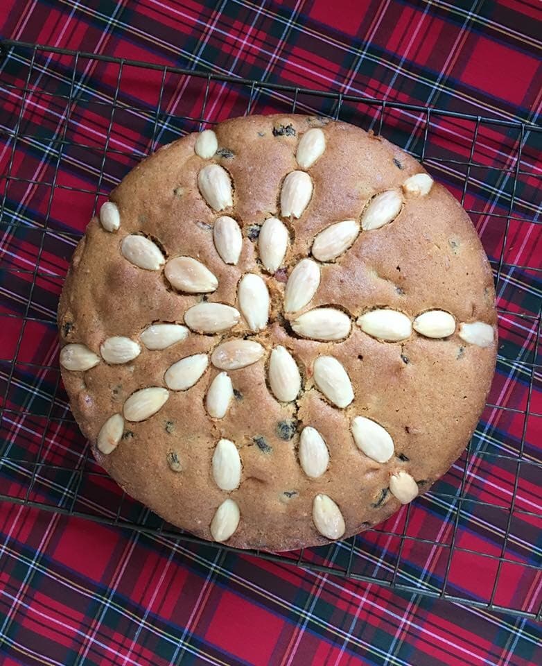 A Dundee Cake sitting on a black wire rack and tartan tablecloth