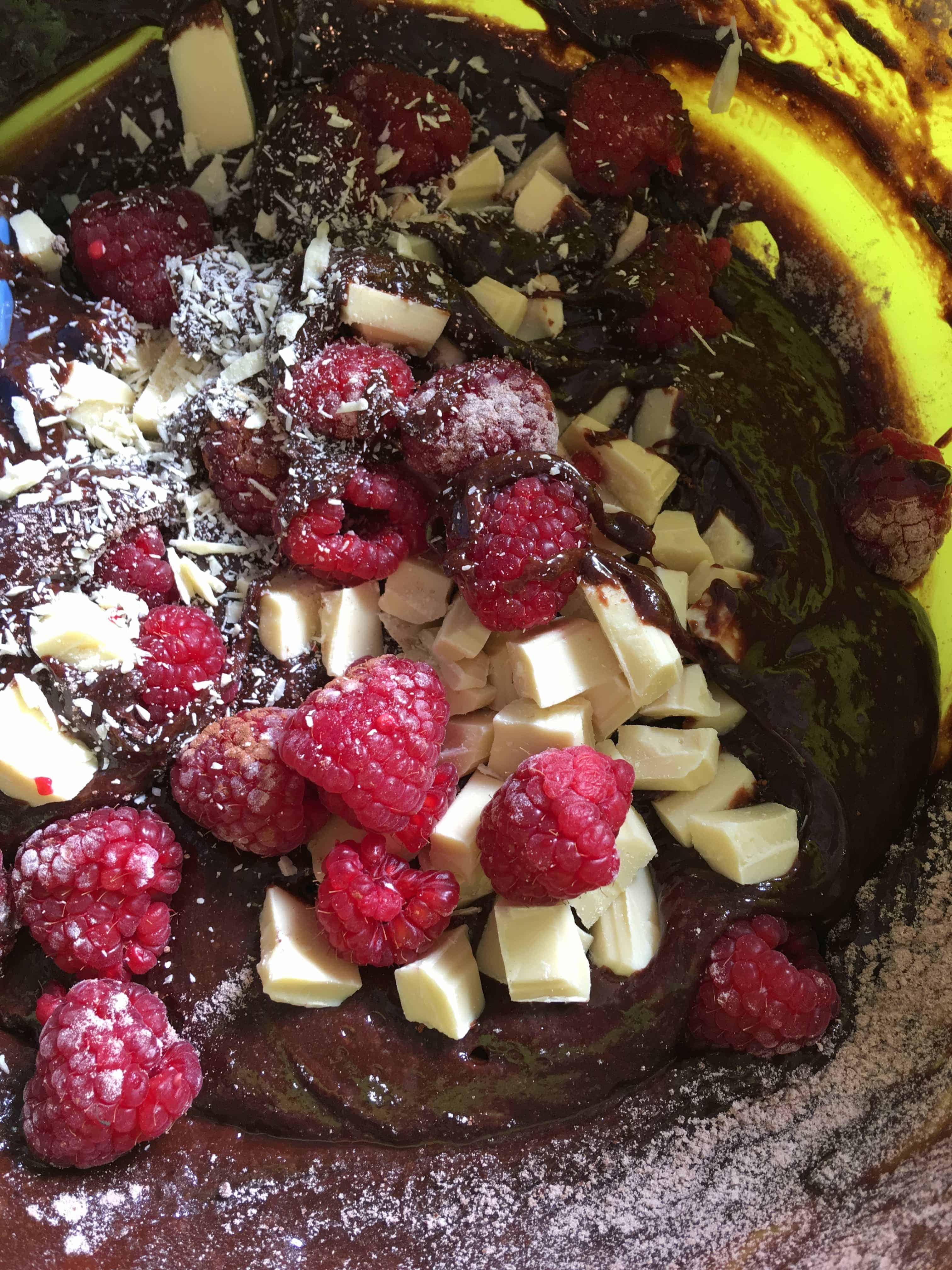 A bowl of brownie batter with white chocolate chunks and fresh raspberries.