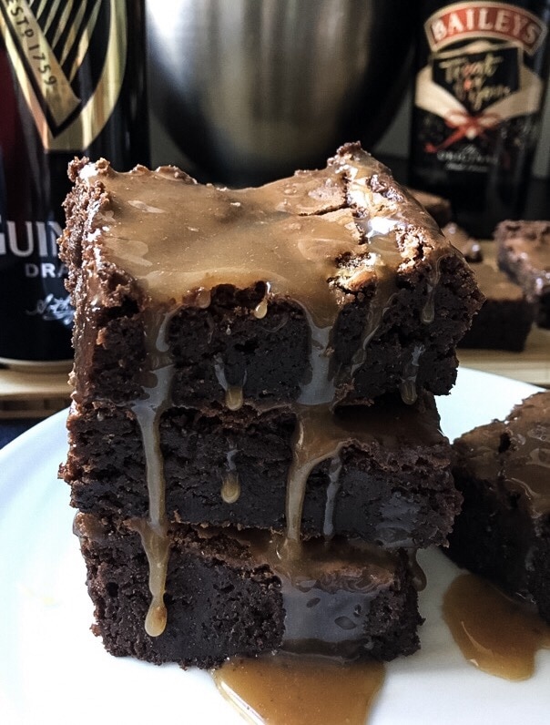 A close up picture of Guinness brownies with salted caramel Guinness Baileys glaze. A tower of brownies with Baileys salted caramel sauce dripping down the sides.