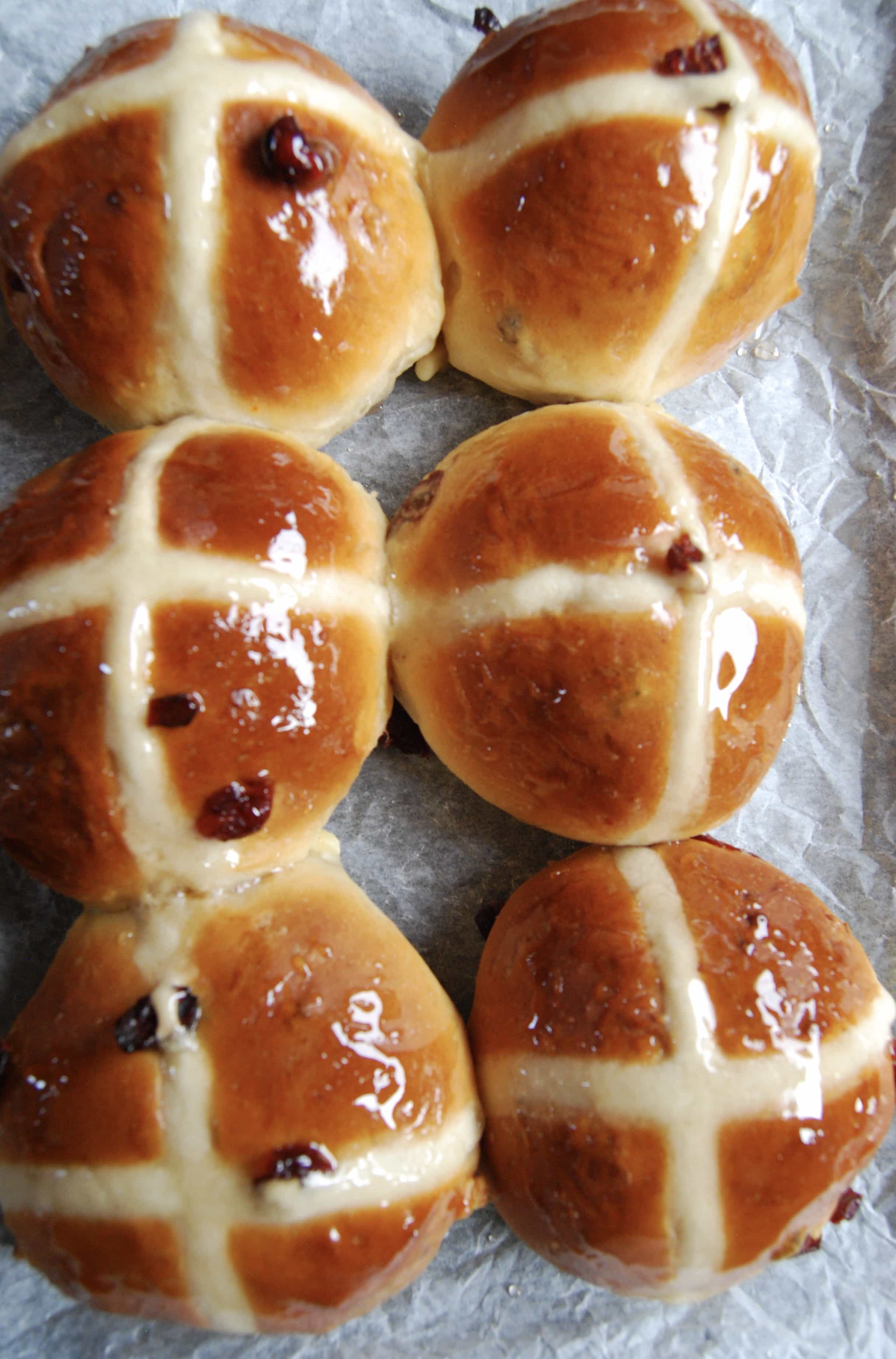 A tray of freshly baked hot cross buns with a shiny sugar glaze.