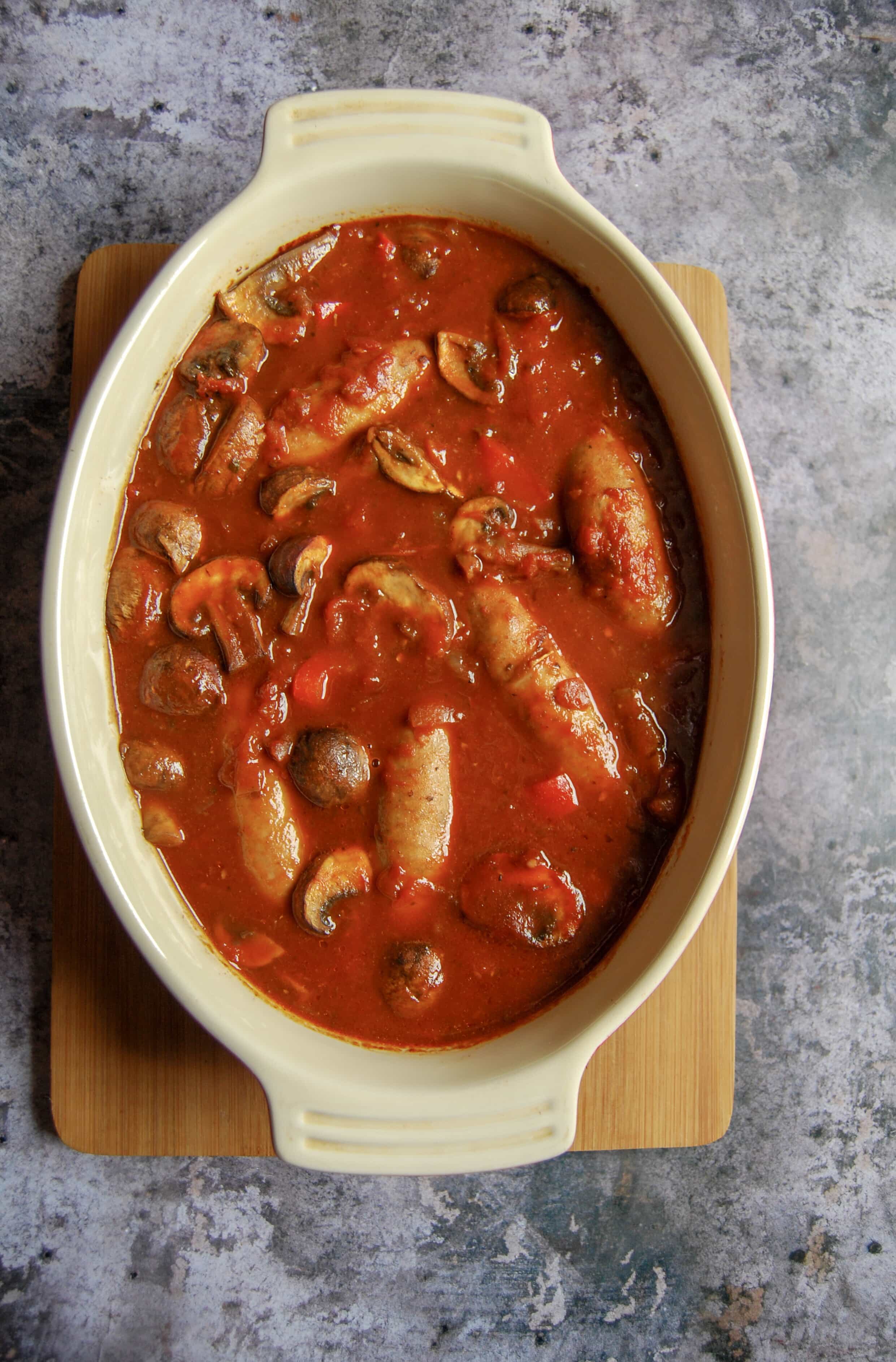 A sausage casserole in a rich tomato sauce with mushrooms, onions and red peppers in a casserole dish.