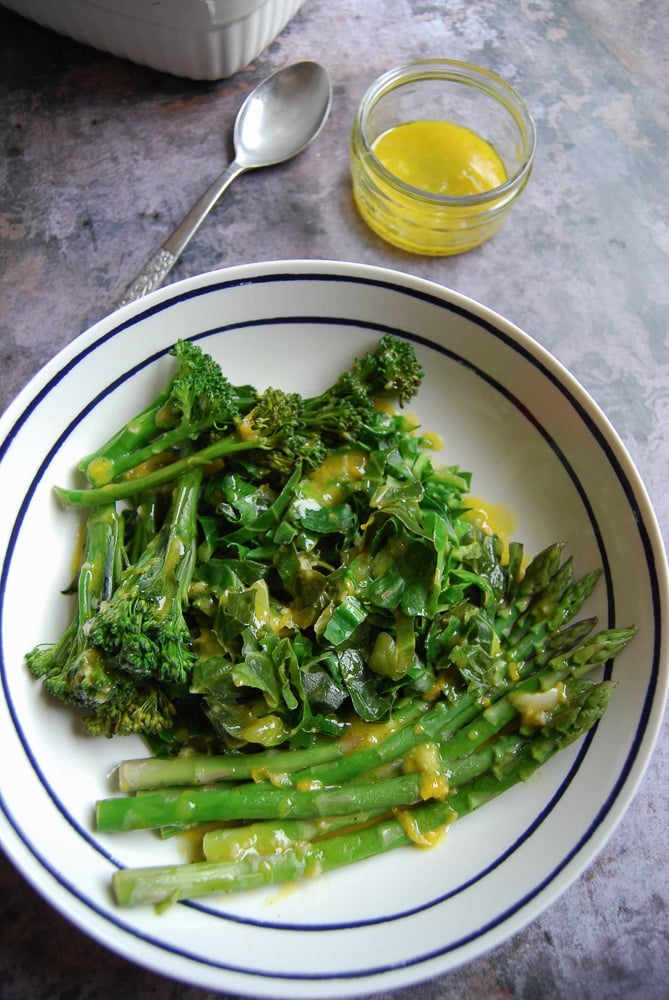 A bowl of spring greens coated in a lemon mustard dressing on a grey background 