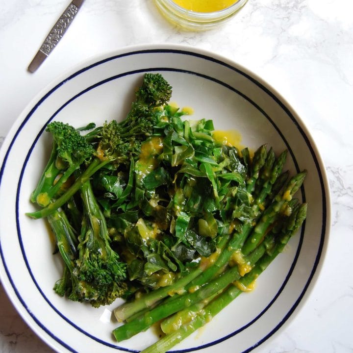 A flatlay photo of a bowl of Spring Greens with lemon and mustard dressing on a marbled white background.