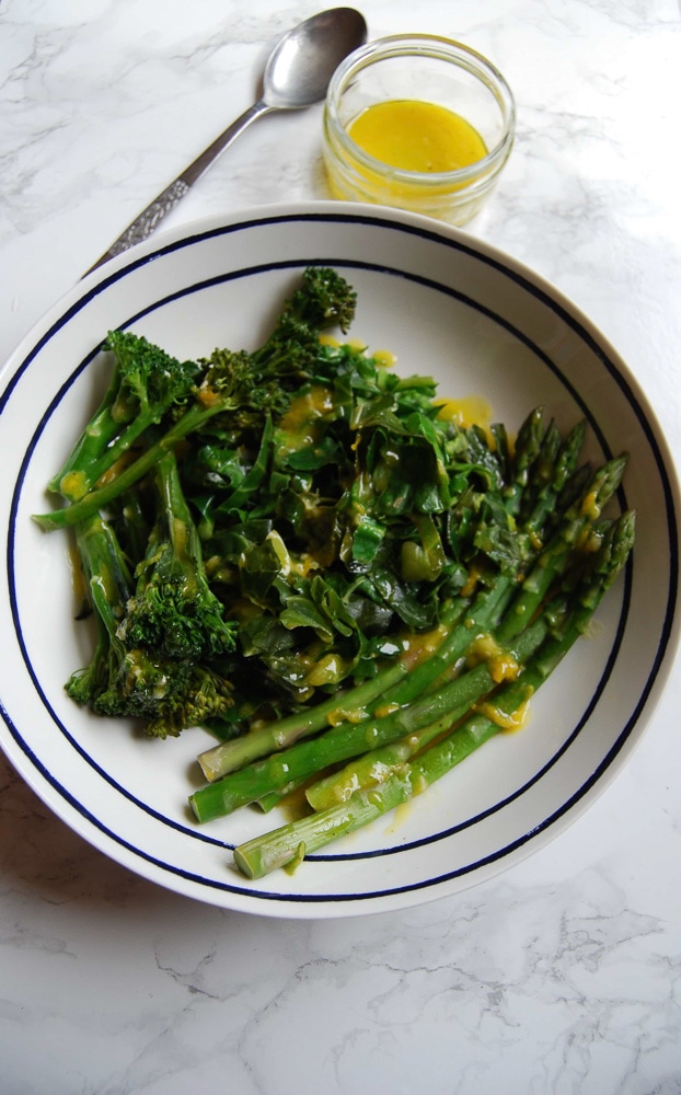 A bowl of fresh Spring greens in a white and blue bowl with a lemon and mustard dressing 