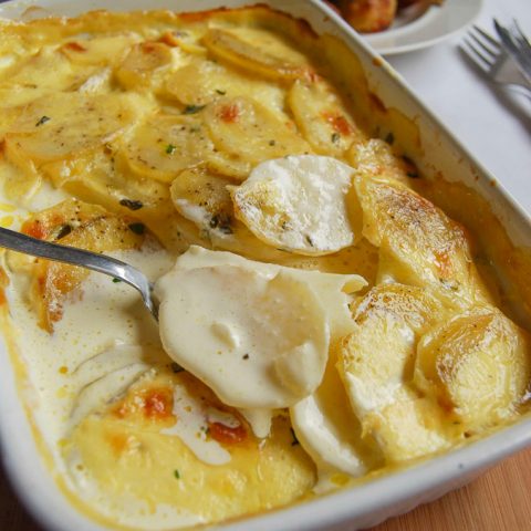 A dish of Dauphinois Potatoes with a roast leg of lamb in the background.