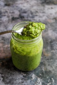 A close up photo of a jar of wild garlic pesto on a grey background.