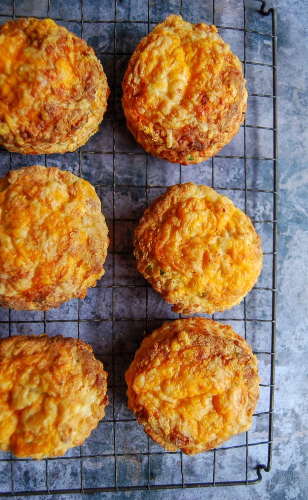 A flatlay close up photograph of six cheese scones on a black wire cooling rack.