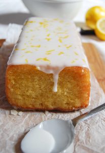 A close up picture of an easy lemon drizzle cake topped with white icing and lemon zest.