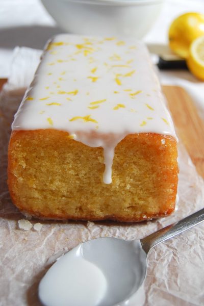 A close up picture of an easy lemon drizzle cake topped with white icing and lemon zest.