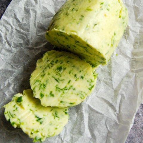 A photo of a log of Wild Garlic Butter, sliced into rounds on a sheet of baking parchment.