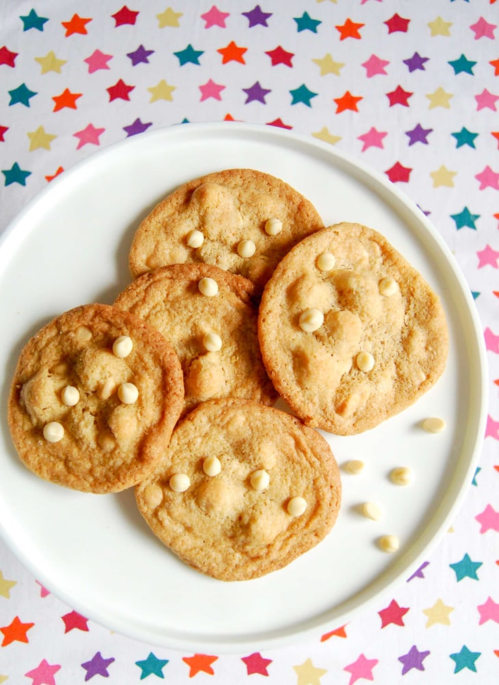 A flatlay picture of white chocolate macadamia nut cookies on a white cake stand.